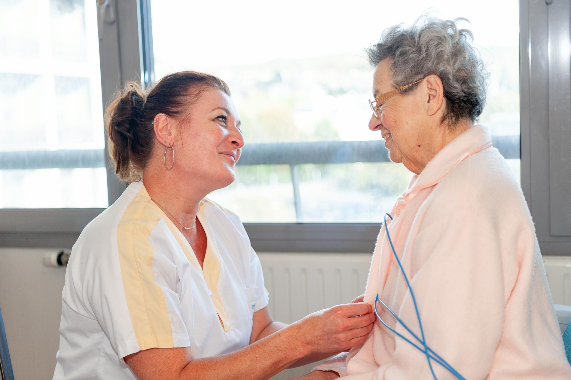 Une aide-soignante et une patiente âgée se regardent affectueusement